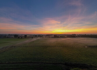 Obraz premium This wide-angle photograph captures the tranquil beauty of a sunrise spreading its warm glow over a lush pasture. The horizon is adorned with an array of colors, ranging from deep purples to fiery