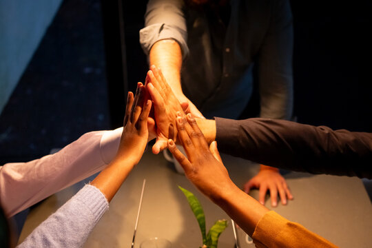 The image displays a group of hands from individuals of varying ethnicities engaging in a collective high-five above a meeting table, highlighting a moment of team success or agreement within a