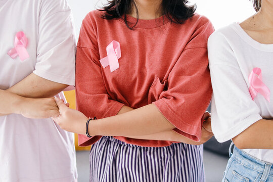 Women holding each other hands and wearing pink ribbon on their chest. Concept of solidarity, support and breast cancer awareness
