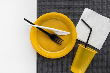 Yellow crockery on a black and white background. Still life with disposable tableware. Plastic recycling.