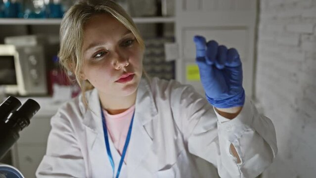 A young blonde woman scientist examines a microscope slide in a laboratory setting, showcasing professionalism and focus.