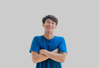 A young Asian man in his 20s wearing a blue t-shirt stands confidently with his arms crossed over his chest, isolated on a gray background. Positive person.