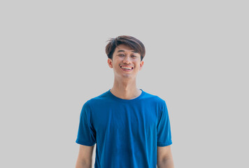 A young Asian man in his 20s wearing a blue t-shirt smiling happily isolated on gray background. The concept of being happy just by smiling. Positive person.
