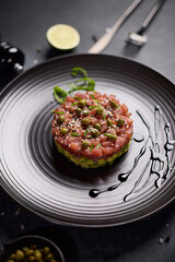 Tuna and avocado tartare with sesame seeds and capers on a dark ceramic plate