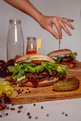 Delicious homemade burger with vegan patty and bun, beautifully arranged on a wooden board with tomato, cucumber, lettuce and burger sauce with peppercorns