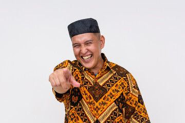 Indonesian man wearing a batik shirt and a kopiah hat chuckling poking fun at someone. Isolated on...