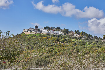 Fototapeta na wymiar Rocky hill with a dirt road in front under a blue sky with white clouds and a modern villa on top