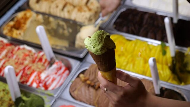 Seller carefully fills waffle cone with different flavors of ice cream from tray. Sweet cone is perfect for serving up cool treat during summer. In crispy cone, ice cream looks especially appetizing.