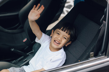Little Asian boy waving goodbye while sitting in the passenger seat, ready to travel by the car.