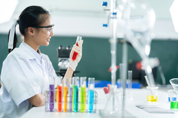 Fototapeta premium Side view of Asian female doctor researching a vaccine in a biolab holding a red test tube as medicine. Do scientific work in medical and pharmaceutical industry companies and use microscopes.