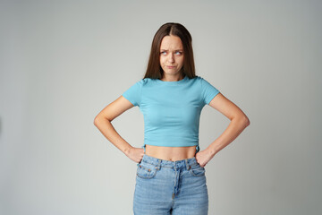 Portrait of sad displeased offended young woman in blue T-shirt on gray background