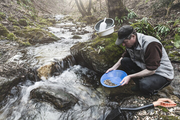 Outdoor adventures on river. Gold panning. Man holding a gold pan is looking for gold in a mountain creek