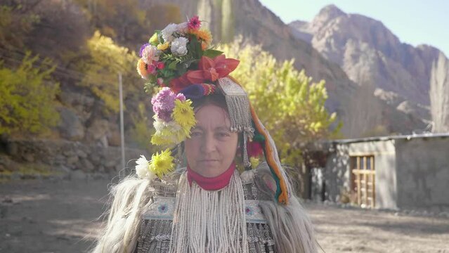 An old Indigenous woman or tribal female wearing ethnic costume or fancy attire standing and looking at camera during a religious ceremony in an Aryan village called Darchik in Upper Himalayas.