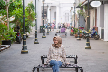 happy asian muslim woman sitting on the bench and roaming around kota lama or old city area,...