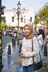 happy asian muslim woman standing beside the street and smiling. roaming around kota lama or old...
