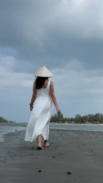 Vietnamese hat on head Young woman on an empty beach in a white dress walks along the sand holding her shoes, shot on RED EPIC. High quality 4k footage