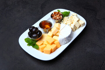 Cheese platter. Different kinds of cheese on a white plate. Honey, nuts and olives on a plate with...