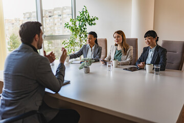A diverse group of multi-ethnic businesswomen sit in a corporate office and have a meeting with a business associate - obrazy, fototapety, plakaty
