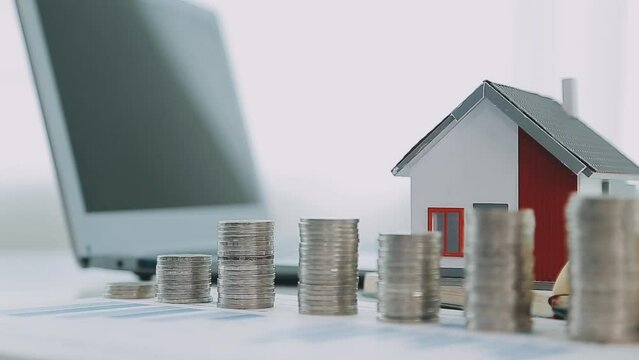 Real estate concept background. House model and coins stack on wooden table, copy space..