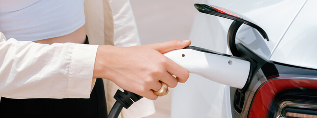 Young woman put EV charger to recharge electric car's battery from charging station. Alternative...