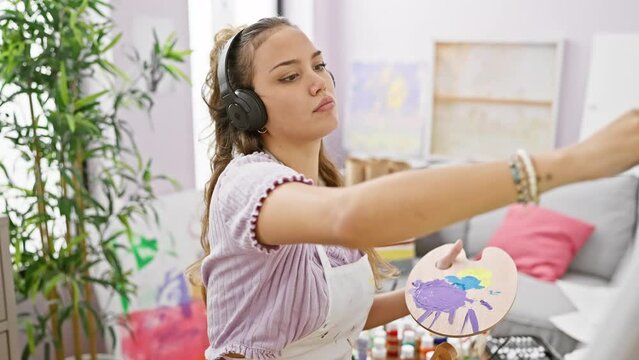 Inspiring art studio scene, confident young beautiful hisapanic woman artist, smiling and immersed in creativity, painting on a canvas, drawing inspiration from the music she is listening to.