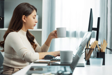 Casual outfit beautiful businesswoman working on desk while holding coffee cup to drink, looking at...