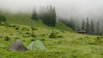 Two tents on a meadow in the mountains, it is raining and foggy. © Niko_Dali