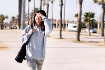 Fototapeta premium smiling young asian woman dressed in casual clothes walking with yoga mat hanging on her arm, sport and healthy lifestyle concept, copy space for text
