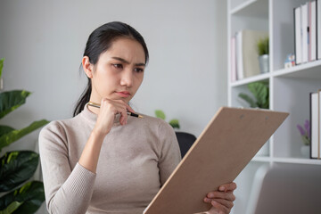 Asian businesswoman feeling tired and stressed over an unsuccessful business while working in a home office decorated with soothing green plants.