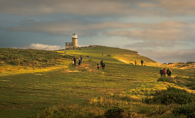 View of lighthouse on hill with people walking towards it on fall  day at sunset