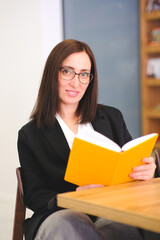 Smiling Woman reading a book in library. Portrait of college girl reading book in library