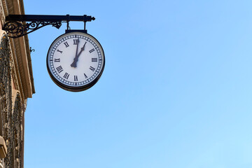 Street clock with Roman numerals on a building and blue clear sky