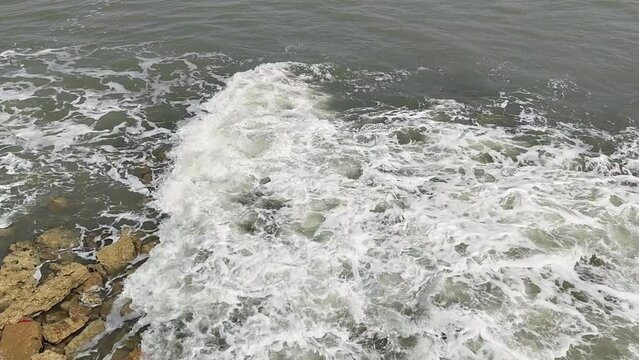 Watch as a wave washes over rocks along the shore in Diu, India, creating a mesmerising display of natural beauty and coastal tranquility.