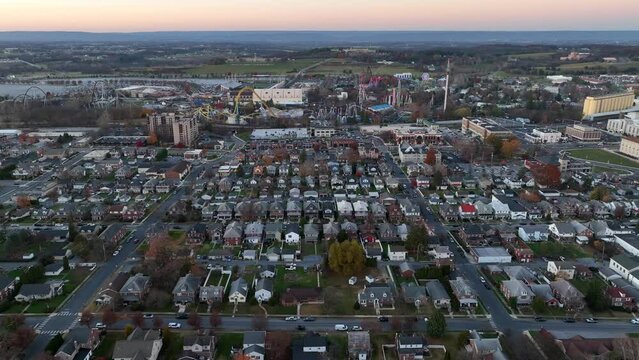 Wide aerial of Hershey, Pennsylvania during autumn sunset. Quaint small town neighborhood with Hershey Park and chocolate factory in distance at dusk.