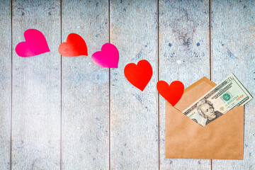 Paper envelope, red, pink paper-cut hearts and American dollars as a gift on a wooden background. Topview pattern for St. Valentines Day