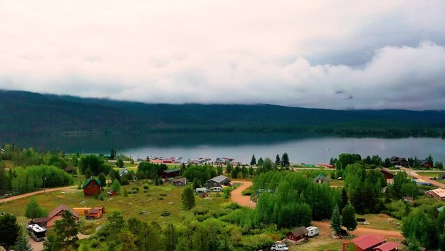 Drone Reviel of a Beautiful Mountain Lake with Cloudy Hills and a Peaceful Clear Body of Water. Aerial Rise Through Trees with Reflection of Clouds on the Glass Calm Water. Boats and Cars Drving