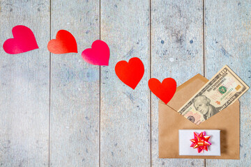 Paper envelope, red, pink paper-cut hearts and American dollars as a gift on a wooden background. Topview pattern for St. Valentines Day