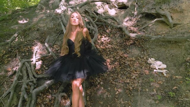 Elegant pretty young ballerina moving among tree roots in forest