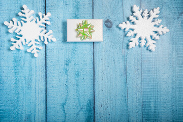 Snowflakes and a present with green ribbon on a light blue wooden background. Christmas winter flatlay with copyspace