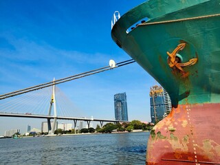 Obraz premium ship in the port, Anchor on large cargo ship's anchor being pulled. Green and red ship, While docked at the pier by large ropes on the river, the building background and transport concept