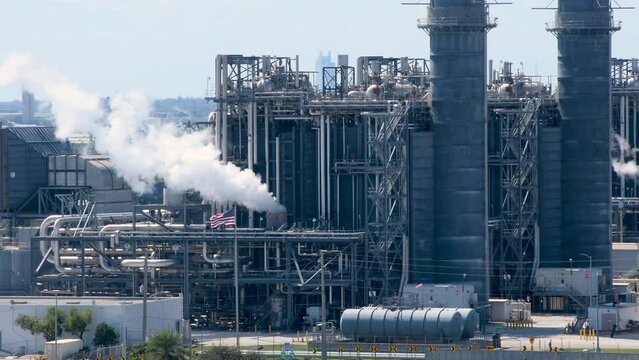 Explore the immense scale of clean energy natural gas plant with billowing white smoke, framed by the USA Flag waving in the video background, reflecting energy innovation and national ethos