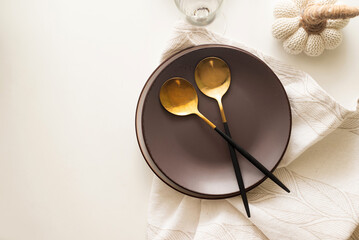 Dinner table setting with white and brown ceramic plates, golden cutlery set and  eucalyptus leaves