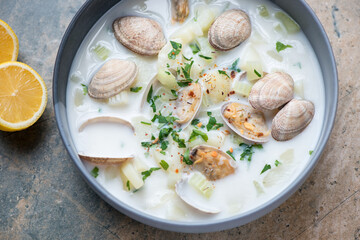 Plate of new england chowder with vongole clams, horizontal shot on a beige and grey granite surface, middle closeup, elevated view