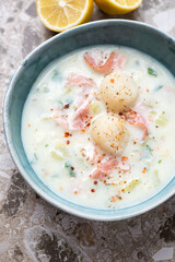 Milky chowder with scallops and bacon in a green bowl, vertical shot on a brown granite surface, middle closeup