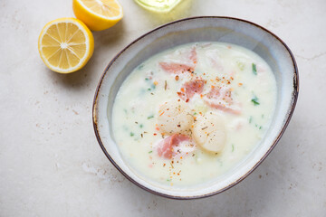 Bowl with scallop and bacon chowder on a light-beige stone background, horizontal shot, elevated view