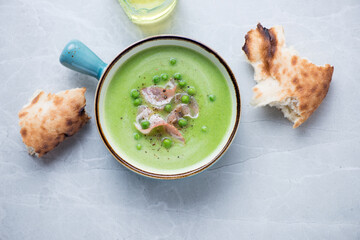 Turquoise serving bowl with green pea and bacon soup, above view on a grey granite background, horizontal shot