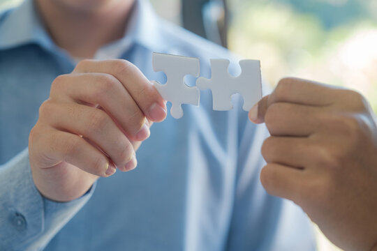 Two People Holding A Puzzle Piece Together. Concept Of Teamwork And Collaboration.