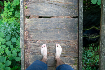 A barefoot man stands on a dangerous wooden bridge over a gorge. Point of view. - 762138760