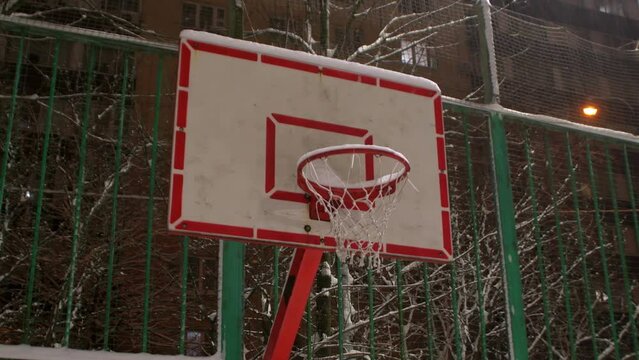 Public basketball court in winter. Close-up of a basketball hoop under the snow.
