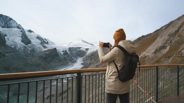 beautiful young woman traveler stands on the observation deck and takes pictures of beautiful views of the mountains and glacier along Majestic Grossglockner Mountain Road in Austria